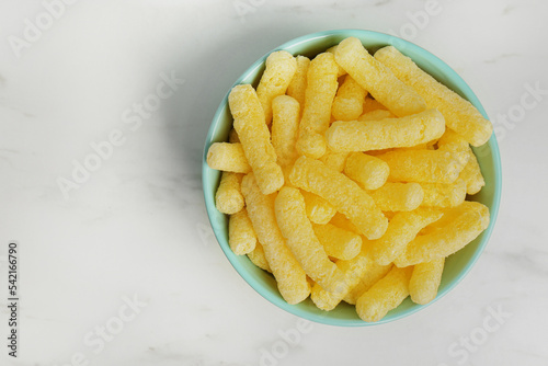 Bowl of delicious crispy corn sticks on white marble table, top view. Space for text photo