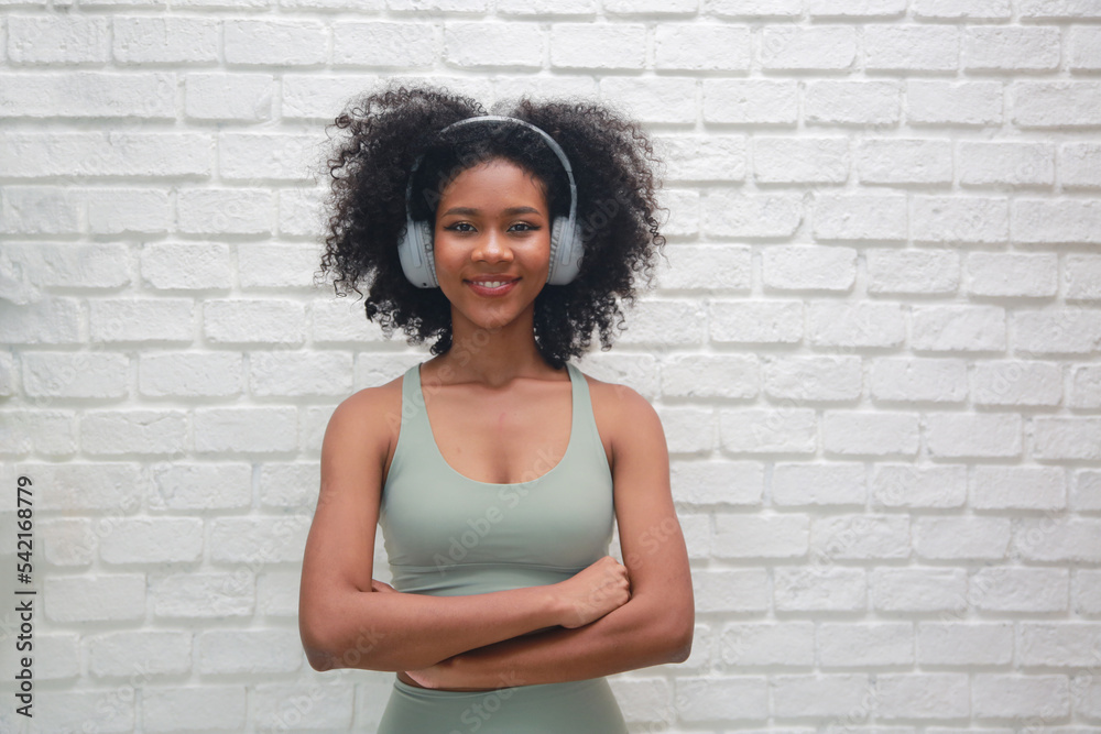 Millennial hipster girl with Afro hair enjoys music podcast in headphones, points fore finger on copy space for your advertising, has excited surprised happy expression