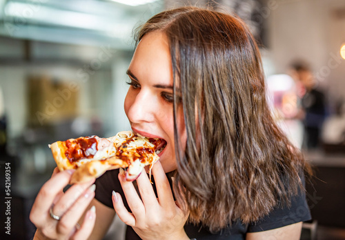 young woman eating slice pizza in cafe