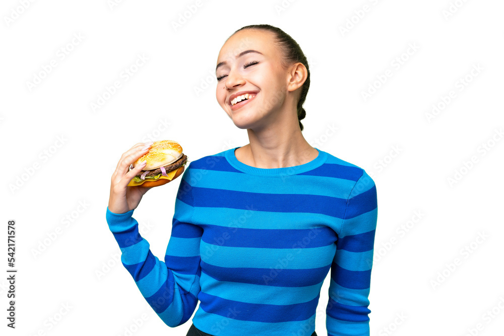 Young Arab woman holding a burger over isolated background laughing Young Arab woman holding a burger over isolated background laughing