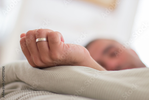 Man sleeping in bed with hand outstretched with wedding ring. Close-up shot of Caucasian mans hand with wedding ring. Man relaxing on weekend, recovering strength. Sleep cycle, engagement concept