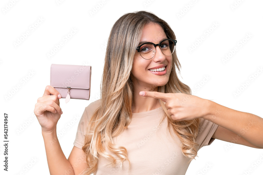 Young Uruguayan woman holding a wallet over isolated background and pointing it