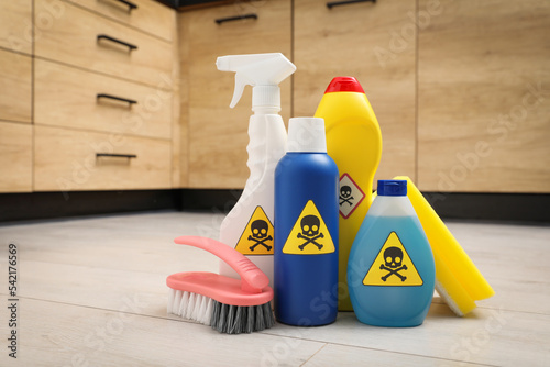 Bottles of toxic household chemicals with warning signs, scouring sponge and brush on floor indoors photo