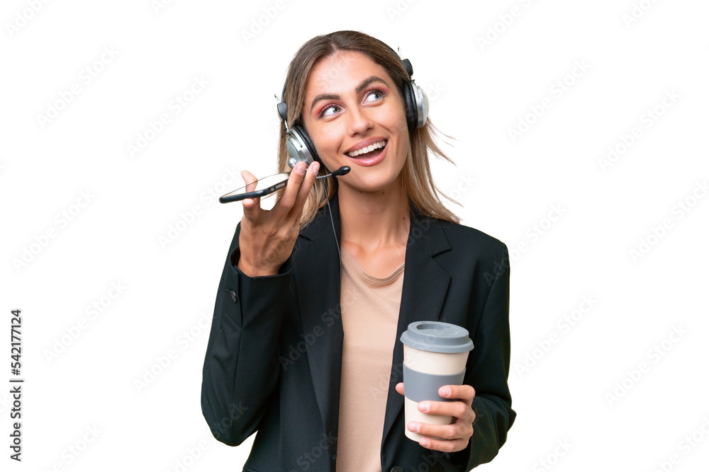 Telemarketer pretty Uruguayan woman working with a headset over isolated background holding coffee to take away and a mobile Telemarketer pretty Uruguayan woman working with a headset over isolated background holding coffee to take away and a mobile