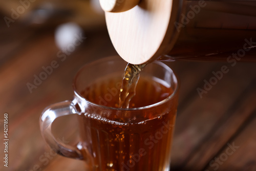 Pouring delicious tea into glass cup on blurred background, closeup