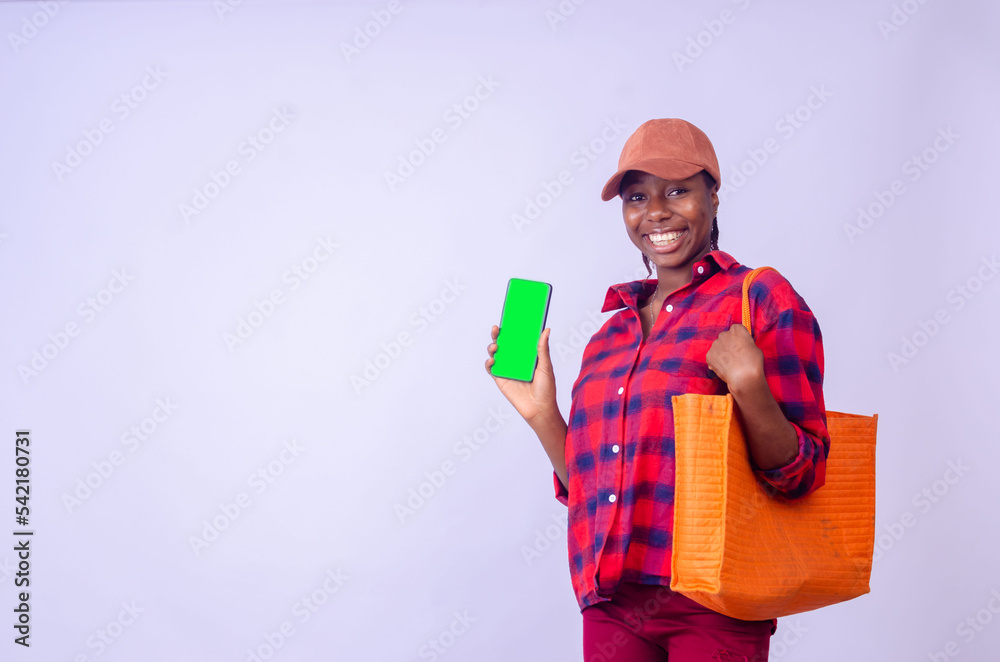 Stylish young african american woman in summer outfit posing with purchases, showing cell phone with green empty screen Stylish young african american woman in summer outfit posing with purchases, showing cell phone with green empty screen