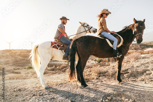 Fototapeta Naklejka Na Ścianę i Meble -  Young couple riding horses doing excursion at sunset - Focus on woman face