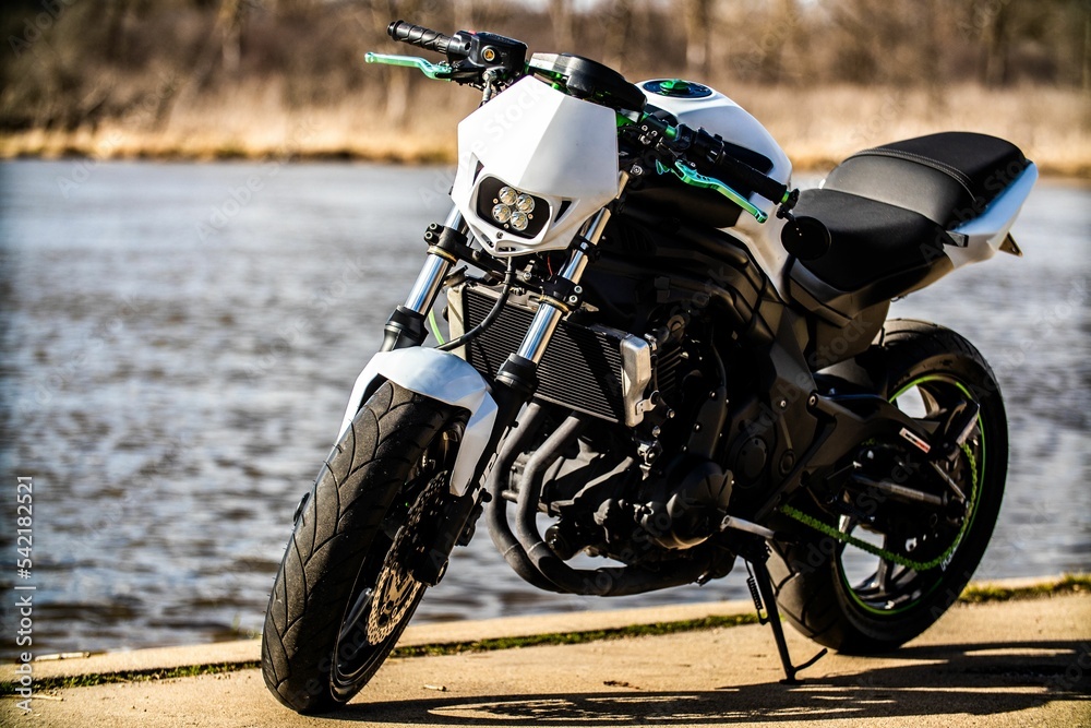 Close-up of a black motorcycle with white details and green lines on lake background on sunny day Close-up of a black motorcycle with white details and green lines on lake background on sunny day