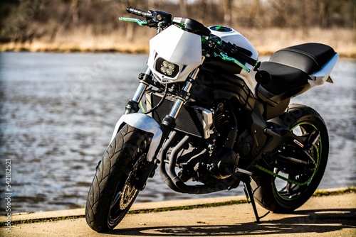Fototapeta Naklejka Na Ścianę i Meble -  Close-up of a black motorcycle with white details and green lines on lake background on sunny day
