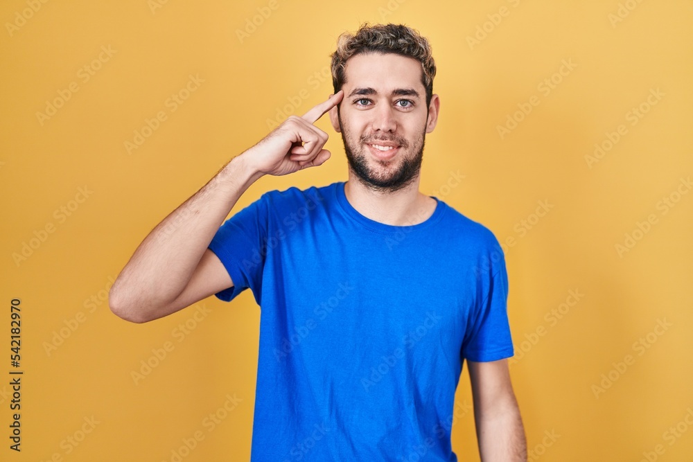 Hispanic man with beard standing over yellow background smiling pointing to head with one finger, great idea or thought, good memory Hispanic man with beard standing over yellow background smiling pointing to head with one finger, great idea or thought, good memory