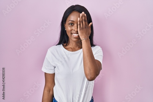 African young woman wearing casual white t shirt covering one eye with hand, confident smile on face and surprise emotion. © Krakenimages.com