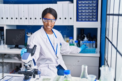 Young african american woman scientist using microscope working at laboratory