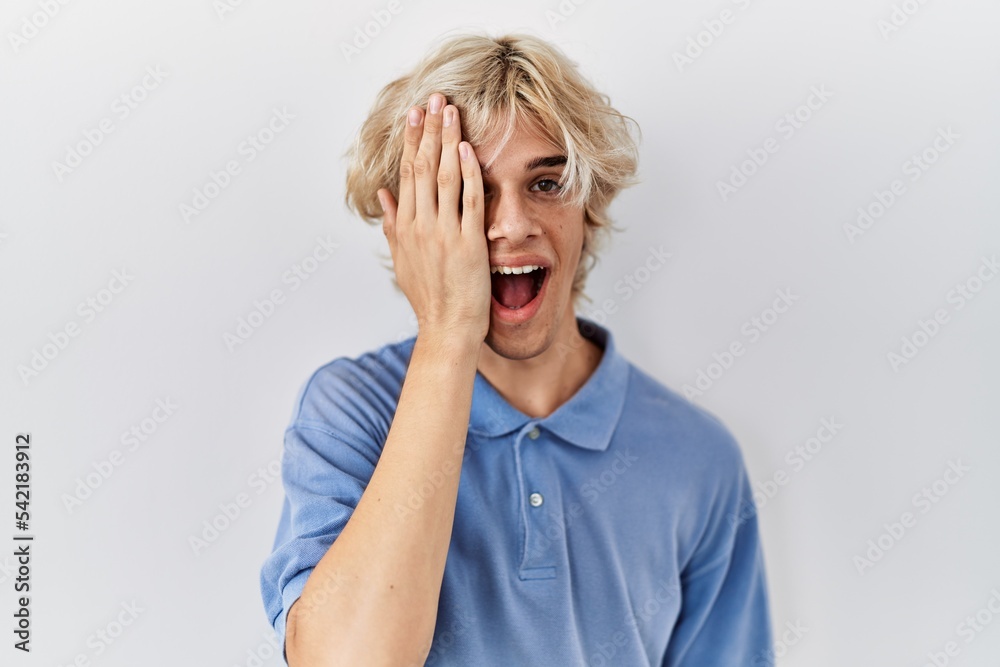Young modern man standing over isolated background covering one eye with hand, confident smile on face and surprise emotion. Young modern man standing over isolated background covering one eye with hand, confident smile on face and surprise emotion.