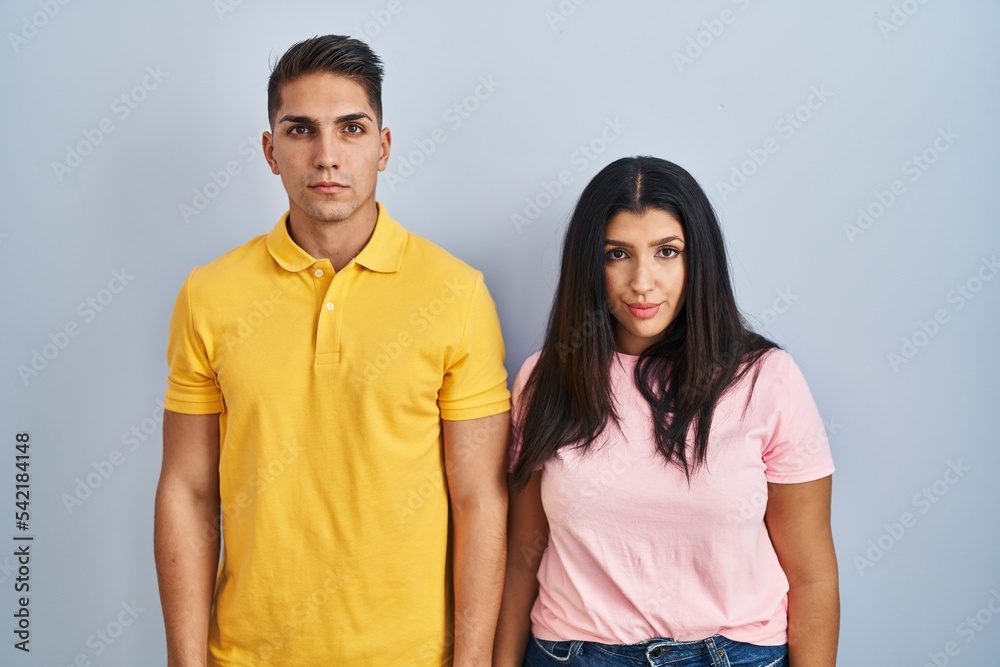 Young couple standing over isolated background relaxed with serious expression on face. simple and natural looking at the camera. Young couple standing over isolated background relaxed with serious expression on face. simple and natural looking at the camera.
