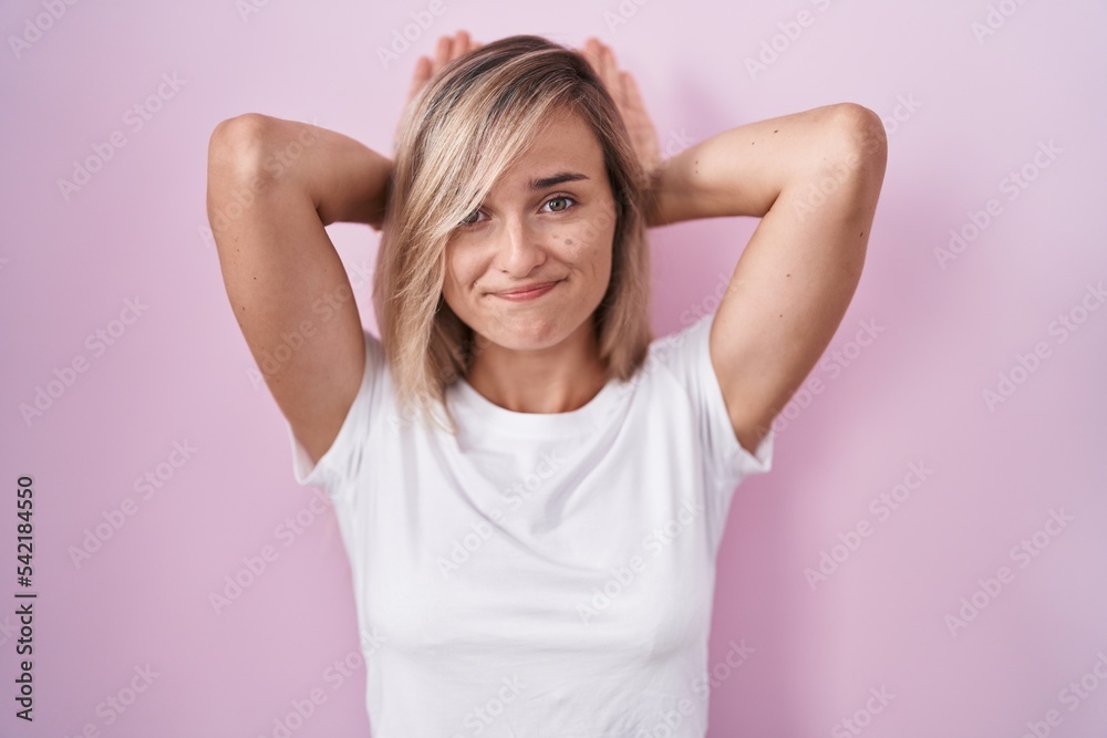Young blonde woman standing over pink background doing bunny ears gesture with hands palms looking cynical and skeptical. easter rabbit concept. Young blonde woman standing over pink background doing bunny ears gesture with hands palms looking cynical and skeptical. easter rabbit concept.