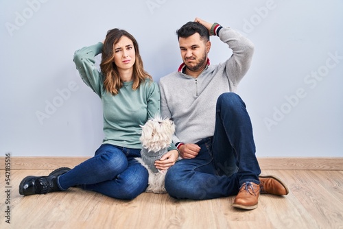 Young hispanic couple sitting on the floor with dog confuse and wondering about question. uncertain with doubt, thinking with hand on head. pensive concept.