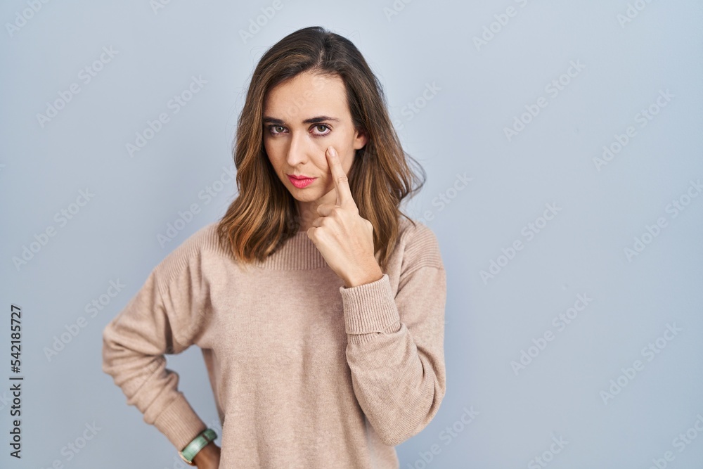 Young woman standing over isolated background pointing to the eye watching you gesture, suspicious expression