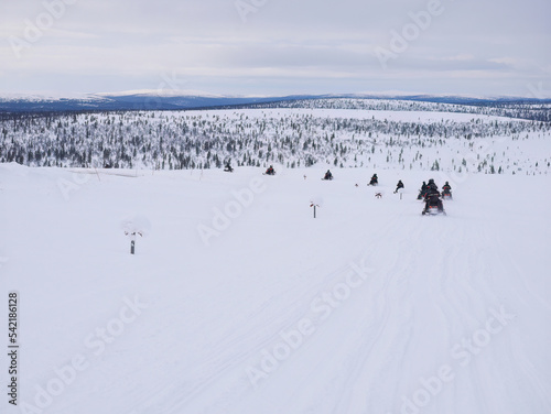 A group of tourists riding Snowmobiles on Glacier through the snowy mountains in Finland, panoramic scene of white snow hills with Pine Tree.