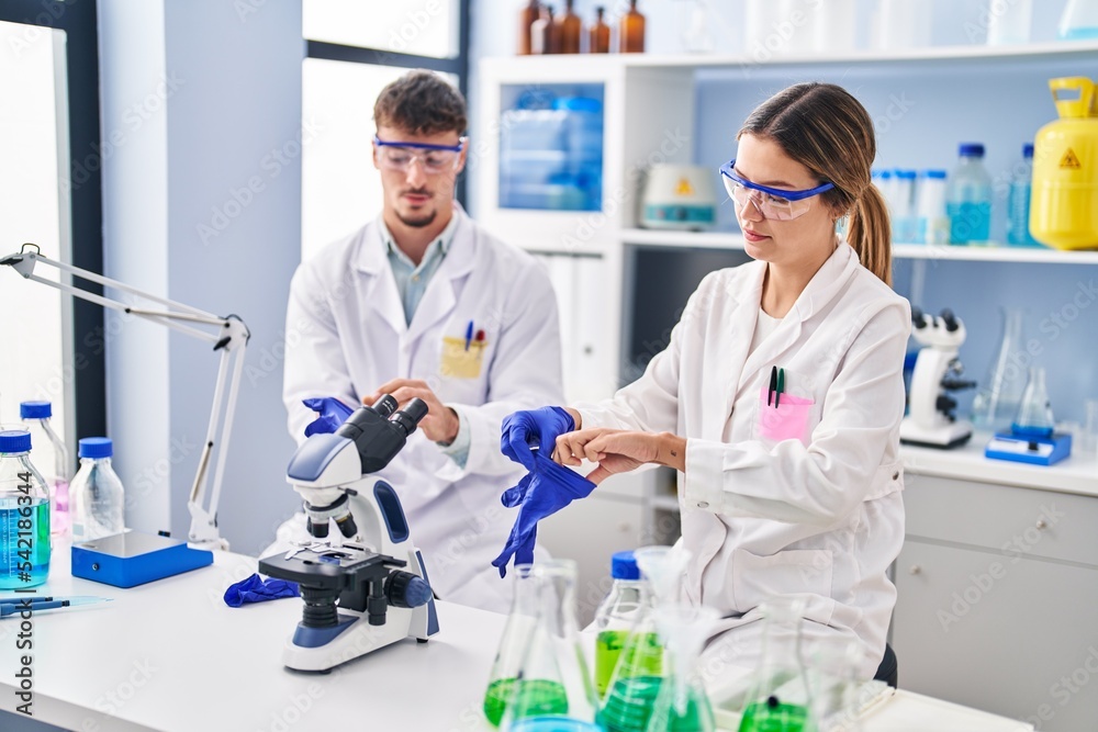 Fototapeta premium Young man and woman scientists workers wearing gloves at laboratory