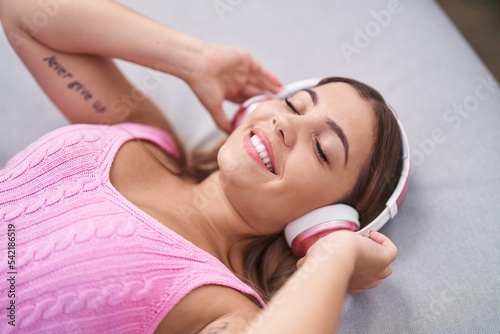 Young beautiful hispanic woman listening to music lying on sofa at home