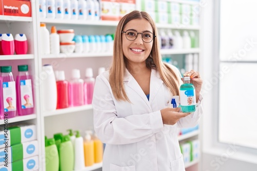 Young blonde woman working at pharmacy drugstore holding syrup smiling with a happy and cool smile on face. showing teeth.