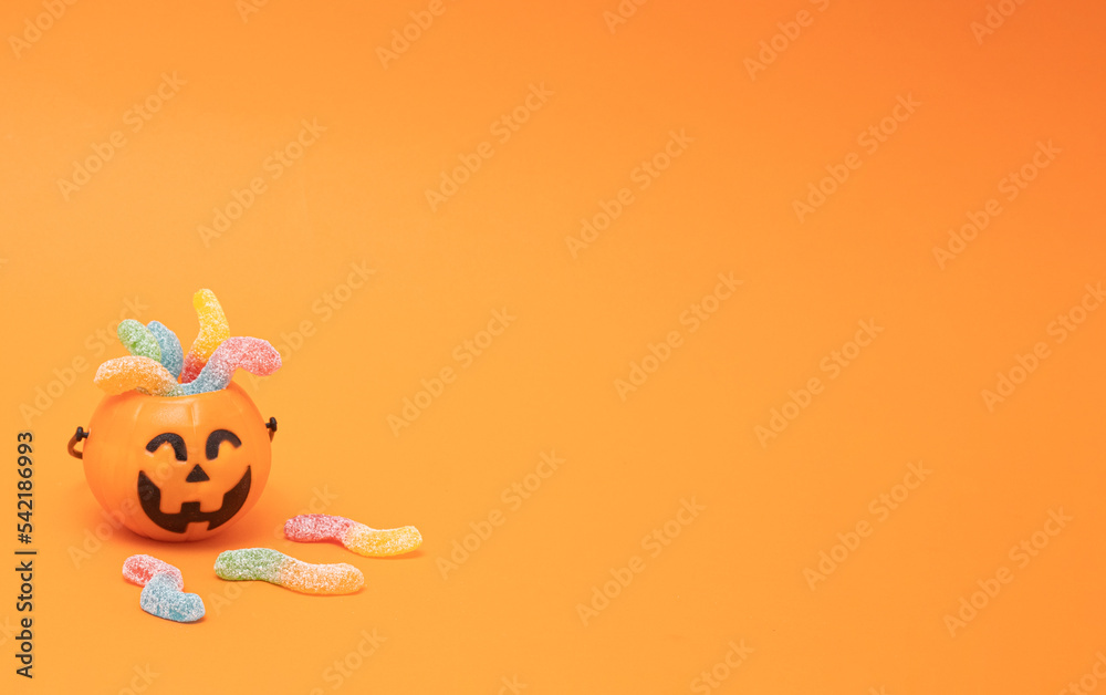 Scary pumpkin with colorful candy worm. Halloween trick or treat copy space on orange background.