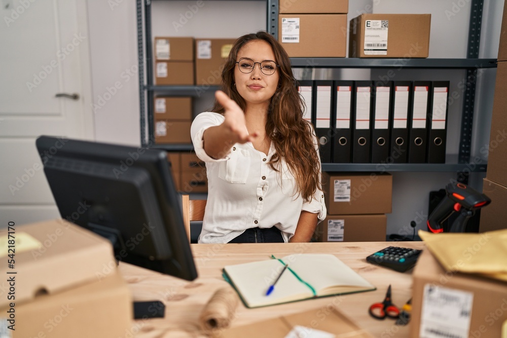 Young hispanic woman working at small business ecommerce smiling cheerful offering palm hand giving assistance and acceptance.