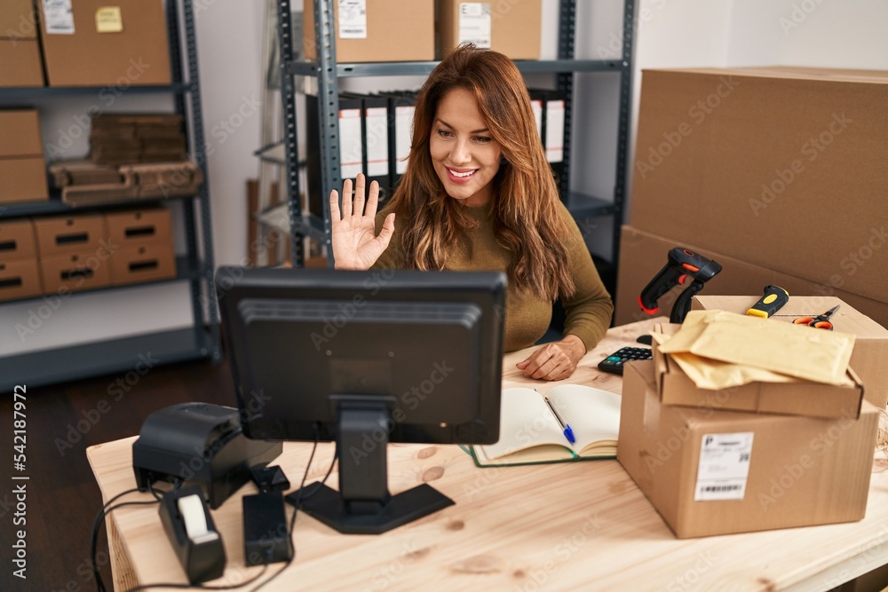 Hispanic woman working at small business ecommerce doing video call looking positive and happy standing and smiling with a confident smile showing teeth Hispanic woman working at small business ecommerce doing video call looking positive and happy standing and smiling with a confident smile showing teeth