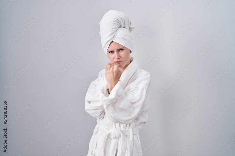 Blonde caucasian woman wearing bathrobe ready to fight with fist defense gesture, angry and upset face, afraid of problem Blonde caucasian woman wearing bathrobe ready to fight with fist defense gesture, angry and upset face, afraid of problem