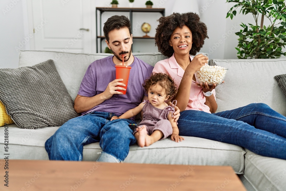 Couple and daughter watching movie sitting on sofa at home Couple and daughter watching movie sitting on sofa at home