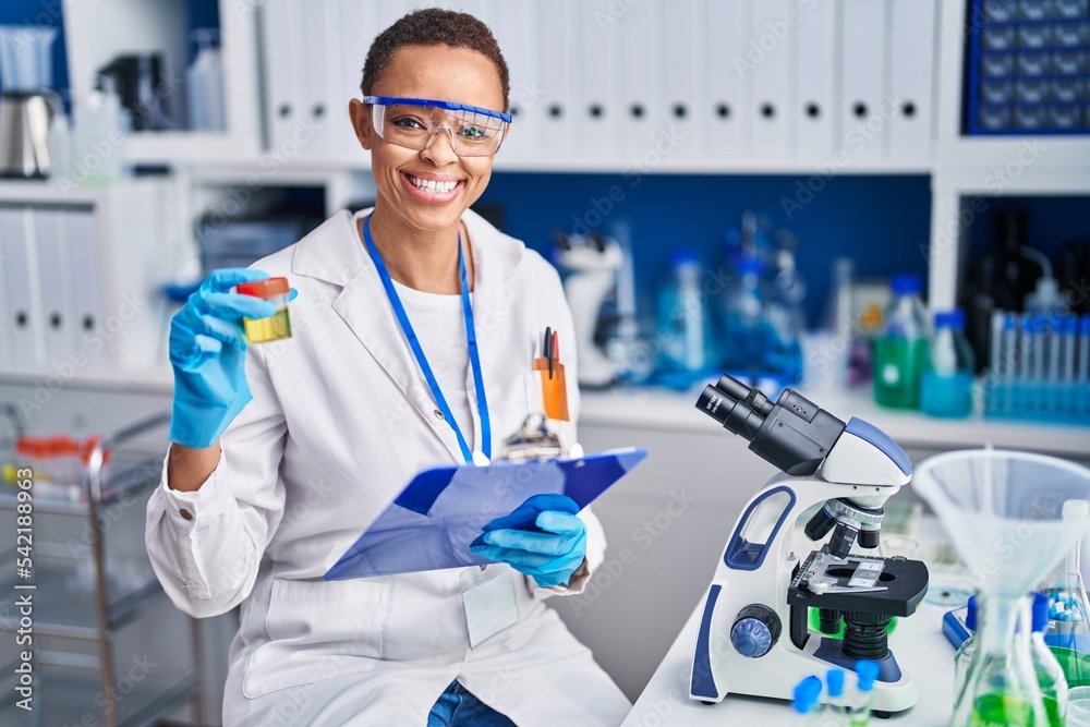 African american woman scientist holding urine test tube reading document at laboratory African american woman scientist holding urine test tube reading document at laboratory