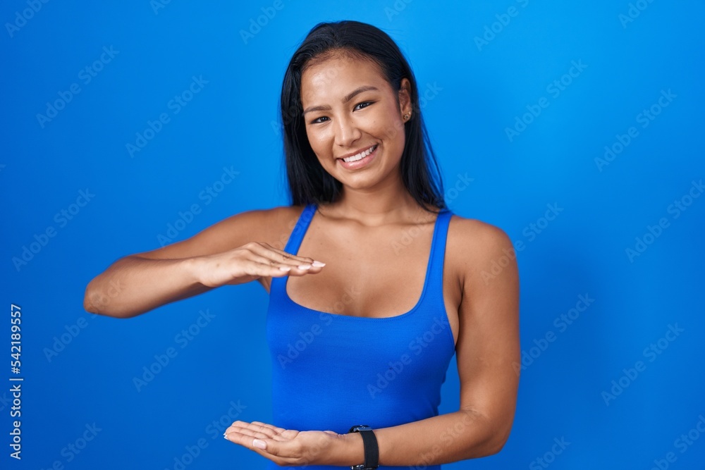 Hispanic woman standing over blue background gesturing with hands showing big and large size sign, measure symbol. smiling looking at the camera. measuring concept. Hispanic woman standing over blue background gesturing with hands showing big and large size sign, measure symbol. smiling looking at the camera. measuring concept.