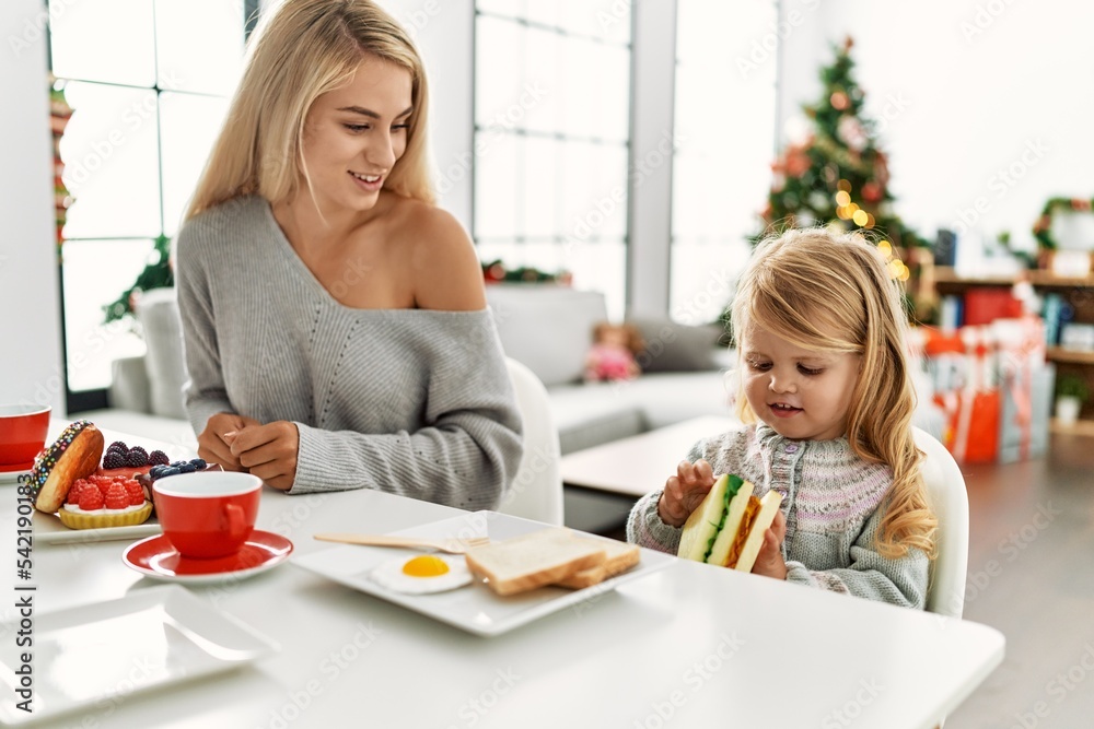 Mother and daughter having breakfast sitting by christmas tree at home Mother and daughter having breakfast sitting by christmas tree at home