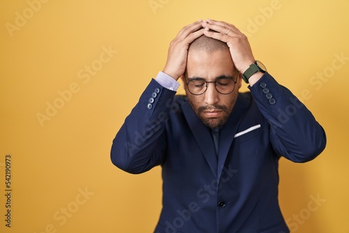 Hispanic man with beard wearing suit and tie suffering from headache desperate and stressed because pain and migraine. hands on head.