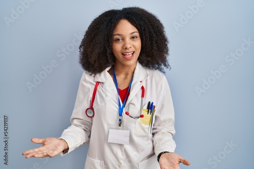 Young african american woman wearing doctor uniform and stethoscope smiling cheerful with open arms as friendly welcome  positive and confident greetings