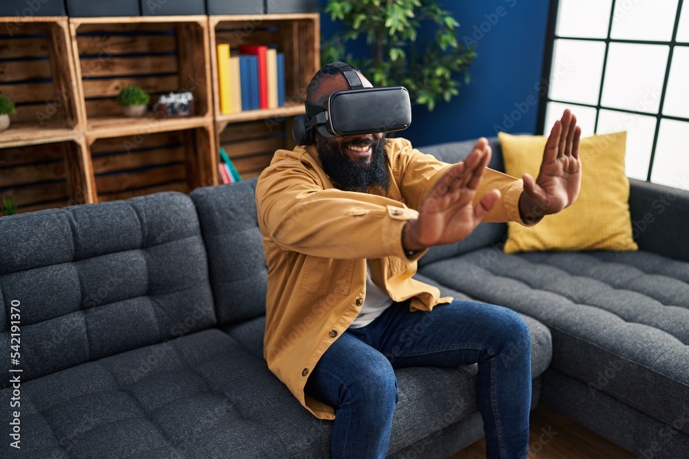 Obraz premium Young african american man playing video game using virtual reality glasses at home