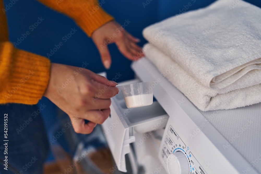 Young beautiful plus size woman pouring detergent on washing machine at laundry room