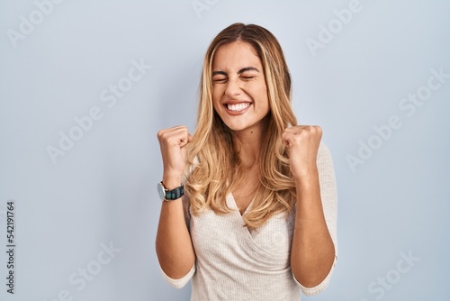 Young blonde woman standing over isolated background excited for success with arms raised and eyes closed celebrating victory smiling. winner concept.