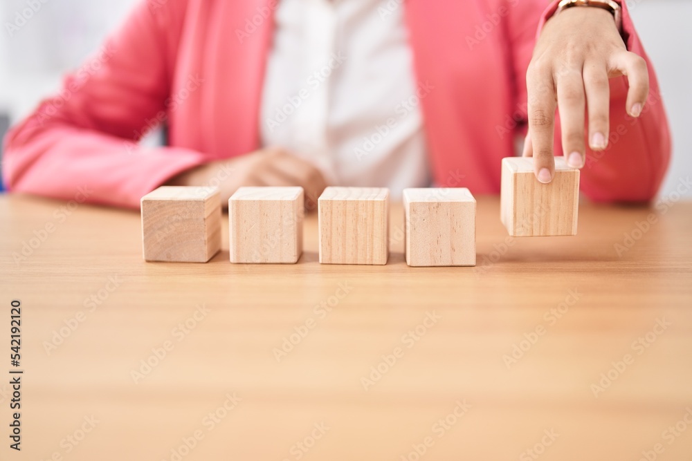 Young beautiful hispanic woman business worker sitting on table with wooden cubes at office Young beautiful hispanic woman business worker sitting on table with wooden cubes at office