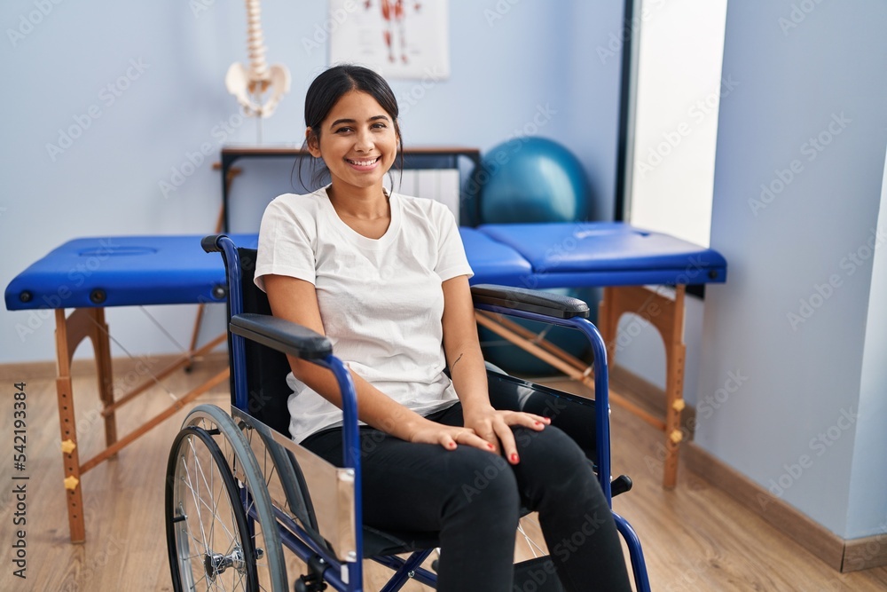 Obraz premium Young hispanic woman sitting on wheelchair at physiotherapy clinic with a happy and cool smile on face. lucky person.
