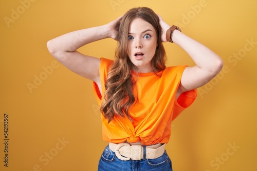 Caucasian woman standing over yellow background crazy and scared with hands on head, afraid and surprised of shock with open mouth