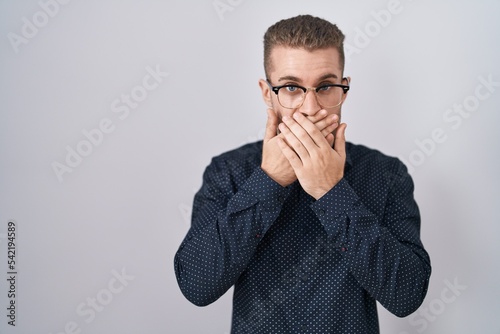 Young caucasian man standing over isolated background shocked covering mouth with hands for mistake. secret concept.