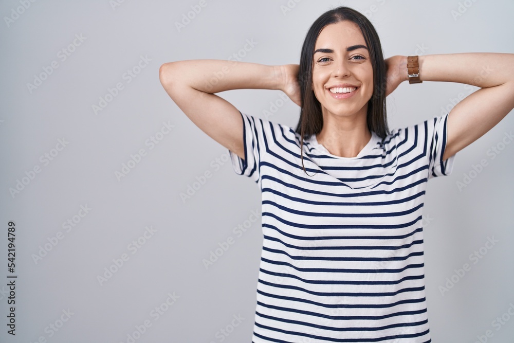 Young brunette woman wearing striped t shirt relaxing and stretching, arms and hands behind head and neck smiling happy Young brunette woman wearing striped t shirt relaxing and stretching, arms and hands behind head and neck smiling happy