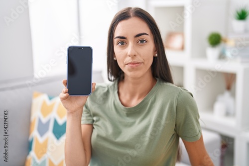 Obraz na plátně Young brunette woman holding smartphone showing blank screen thinking attitude a