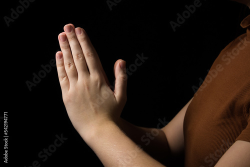 The girl folds her hands in prayer to God on a black background. prayer to God for happiness and a better life. Repent of your sins. Unity with God 