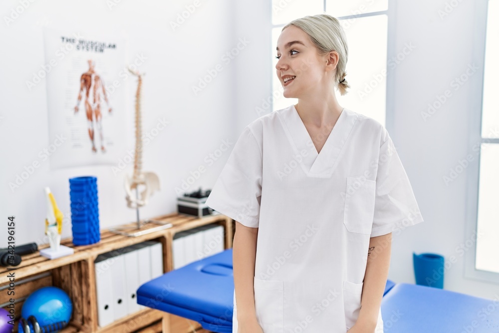 Young caucasian woman working at pain recovery clinic looking away to side with smile on face, natural expression. laughing confident. Young caucasian woman working at pain recovery clinic looking away to side with smile on face, natural expression. laughing confident.