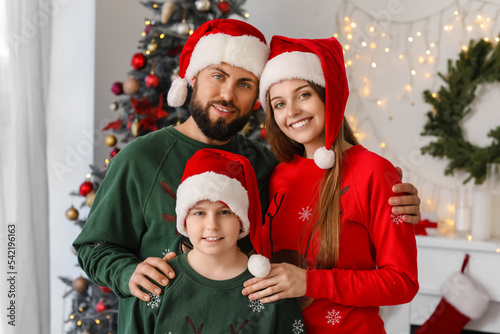 Happy parents with their little son in Santa hats at home on Christmas eve