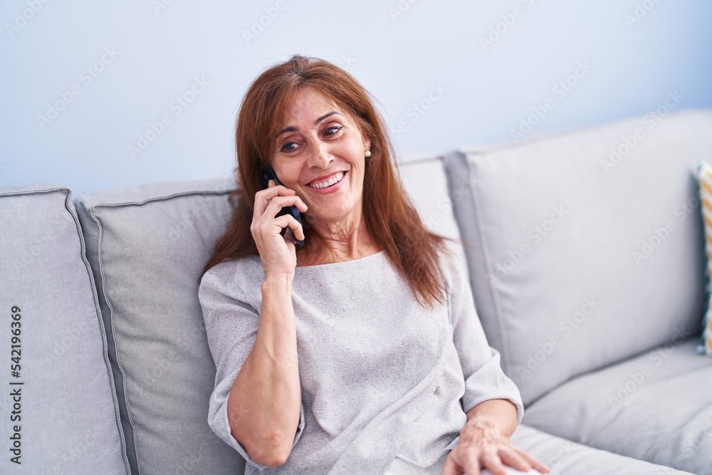 Middle age woman talking on the smartphone sitting on sofa at home Middle age woman talking on the smartphone sitting on sofa at home