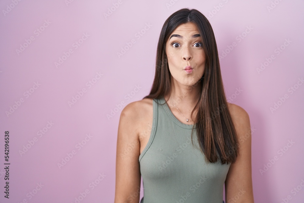 Hispanic woman standing over pink background making fish face with lips, crazy and comical gesture. funny expression. Hispanic woman standing over pink background making fish face with lips, crazy and comical gesture. funny expression.