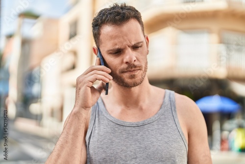 Young hispanic man talking on the smartphone with serious expression at street